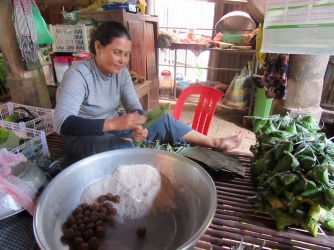 Cette femme prépare des collations avec du riz et du sucre de palme enveloppés dans des feuilles de bananier qu'elle vendra ensuite à l'entrée du temple tout près. Chhlong, Cambodge.