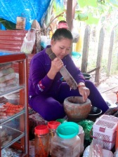 Assise sur une grande structure basse qui ressemble à une énorme table, cette jeune femme prépare une sauce pour accompagner ses plats, Kratie, Cambodge.