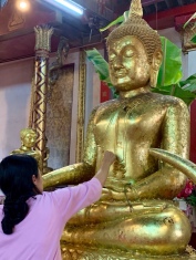 Une femme pose une feuille d'or sur un bouddha. Wat Phanan Choeng Worawihan, Ayutthaya, Thaïlande.